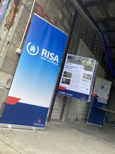 Ein Aufsteller im RISA-Design zeigt das Logo in den halboffenen alten Lagerhallen des PARKS-Geländes
