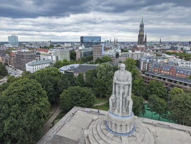 Das Bismarck-Denkmal ist aus der Vogelperspektive zu sehen und steht auf einem erhöhten Sockel in einer von Bäumen umgebenen Parkanlage. Im Hintergrund erstrecken sich die Hamburger Innenstadt