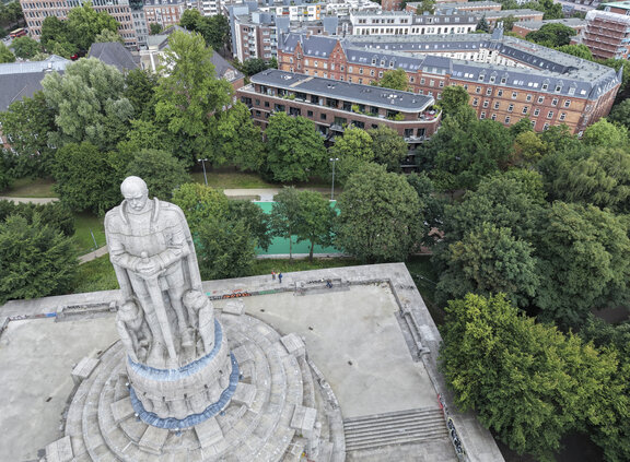 Das Bismarck-Denkmal ist aus der Vogelperspektive zu sehen und steht auf einem erhöhten Sockel in einer von Bäumen umgebenen Parkanlage. Im Hintergrund erstrecken sich die Hamburger Innenstadt