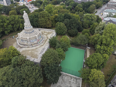 Aus der Vogelperspektive: Rechts liegt der fertige Sportplatz umgeben von Bäumen, links das Bismarck Denkmal.