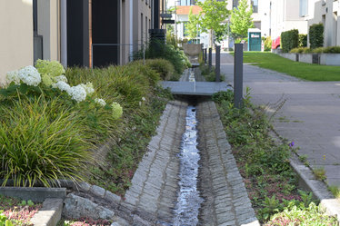 Offene Rinnen entlang der Häuser führen das Regenwasser vom Dach gezielt ab. Kleine Brücken ermöglichen das trockene Überqueren der Rinnen.